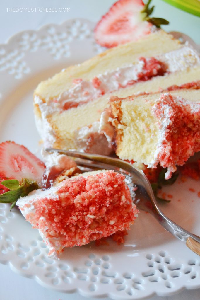 a piece of strawberry shortcake icebox cake sits on a white lacy plate with a fork cutting through the slice.