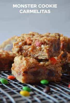monster cookie carmelita bars stacked two high on a black cooling rack with a small scattering of miniature M&M candies around them.