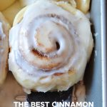 a cinnamon roll in a pan with other cinnamon rolls and a black spatula sits underneath it.