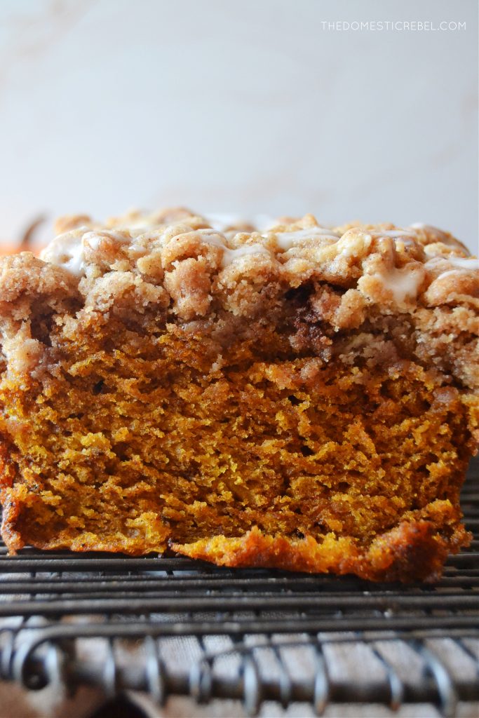a close-up shot of pumpkin streusel bread to show the inside of the bread's texture. the loaf sits on a black cooling rack against a light background.