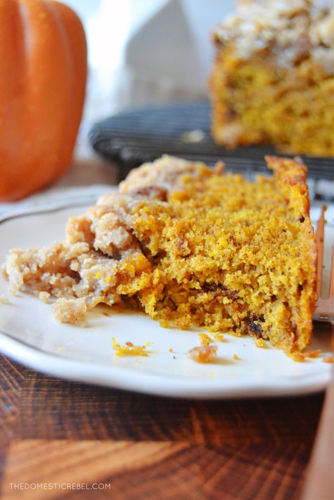 a piece of pumpkin streusel bread on a white plate with a few bites missing from the slice of bread. 