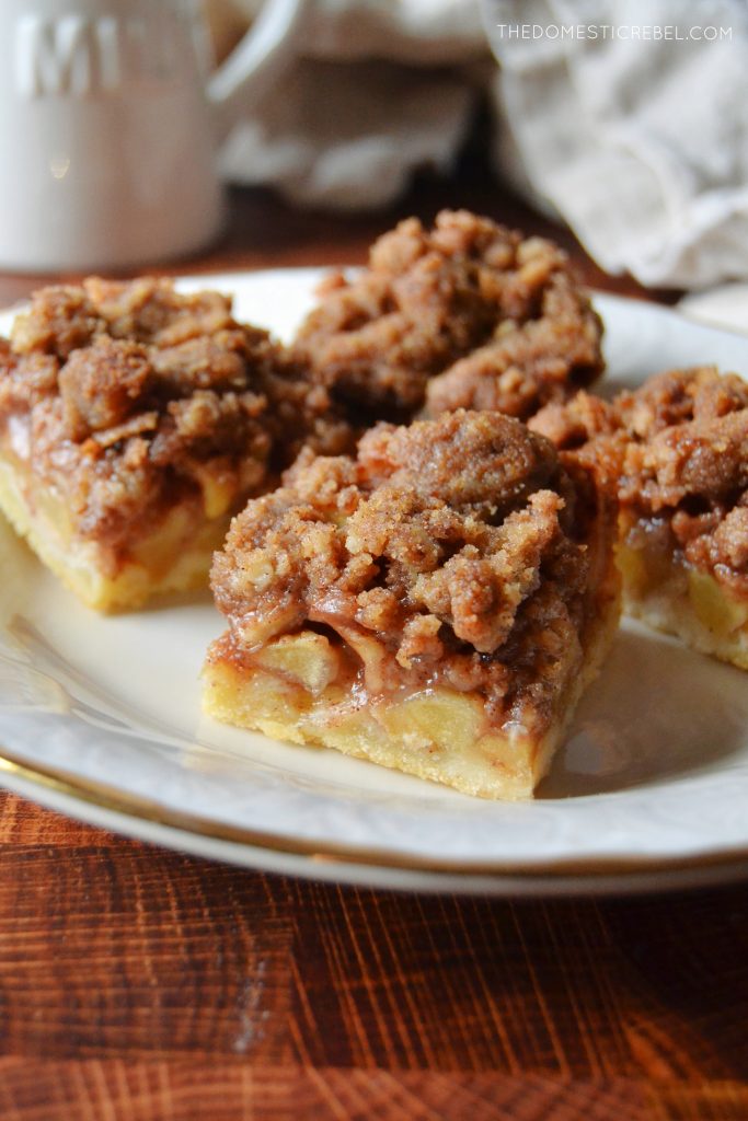 a white plate sits on a butcher block with four dutch apple pie bars on the plate. 