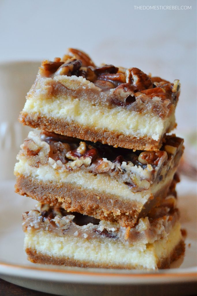 a three-high stack of pecan pie cheesecake bars on a gold-rimmed plate.
