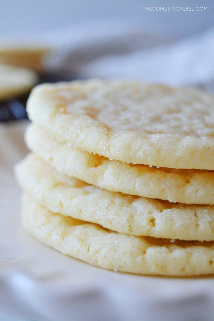 a stack of four sugar cookies on a white scalloped plate, taken up close to show the texture. 