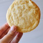 the photographer holding up a sugar cookie to show texture against a light colored background.
